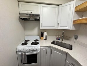 A compact kitchen with white cabinets, a stove, a sink, and a wooden shelf. - Charming studio with AC in the heart of Little Rock (Little Rock)