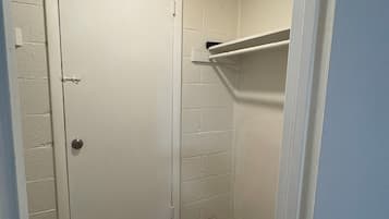 A narrow hallway with a white door, a wooden floor, and a white shelf against the wall.