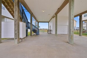 Ein überdachter Außenbereich mit Betonboden, Holzstützen, einer blauen Treppe und Blick auf Häuser im Hintergrund.