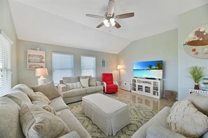 Ein Wohnzimmer mit Deckenventilator, einem roten Sessel, einem Fernseher und einer Kommode mit Dekoration.
