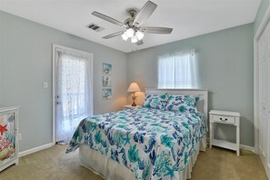 Ein Schlafzimmer mit einem Bett, einem Nachttisch, einem Deckenventilator, einem Fenster mit Vorhängen und einer Tür mit dekorativer Glasscheibe.