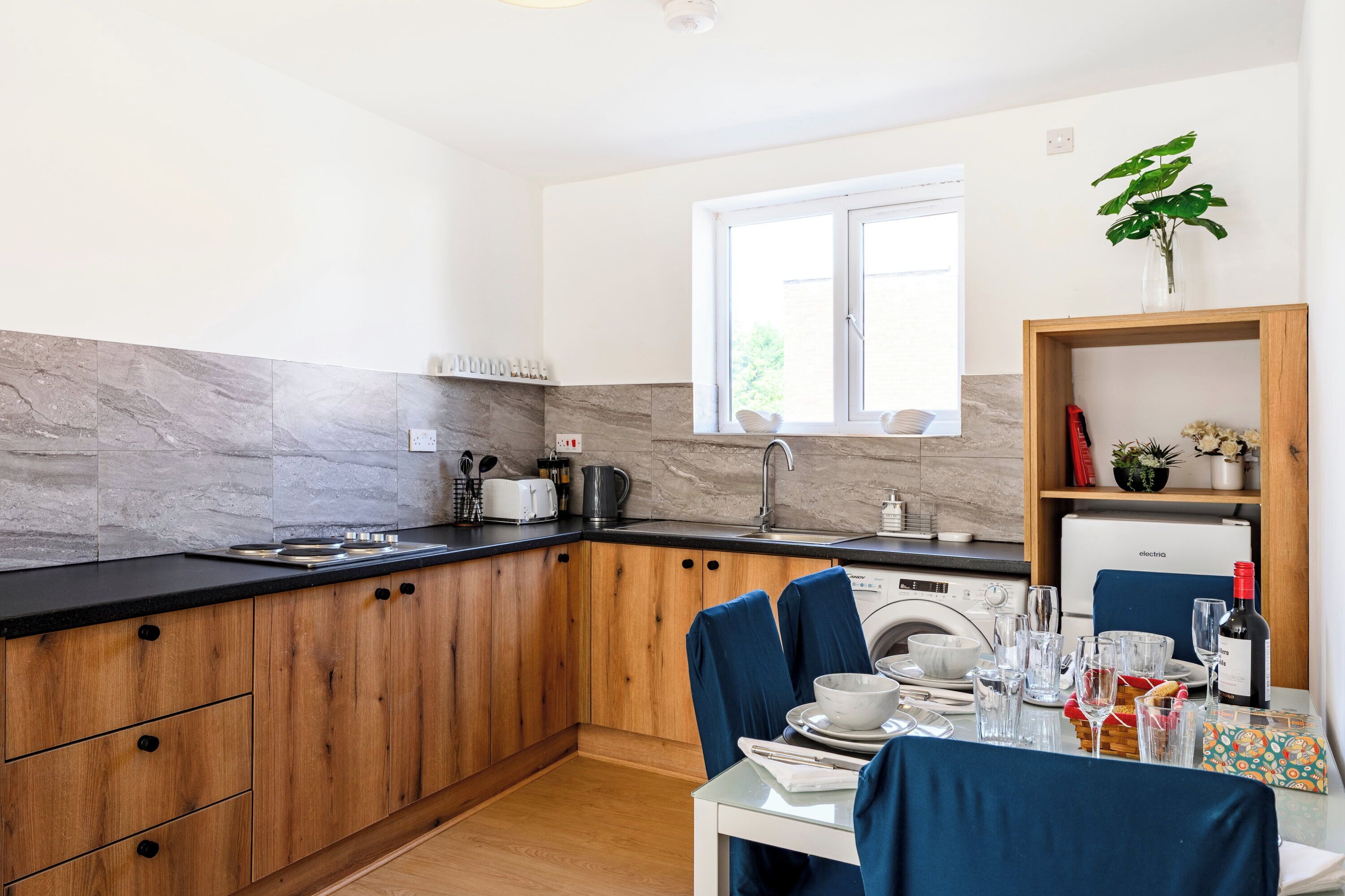 Eine moderne Küche mit Holzausstattung, einem eingebauten Backofen und einem Essbereich mit Tisch für zwei Personen.