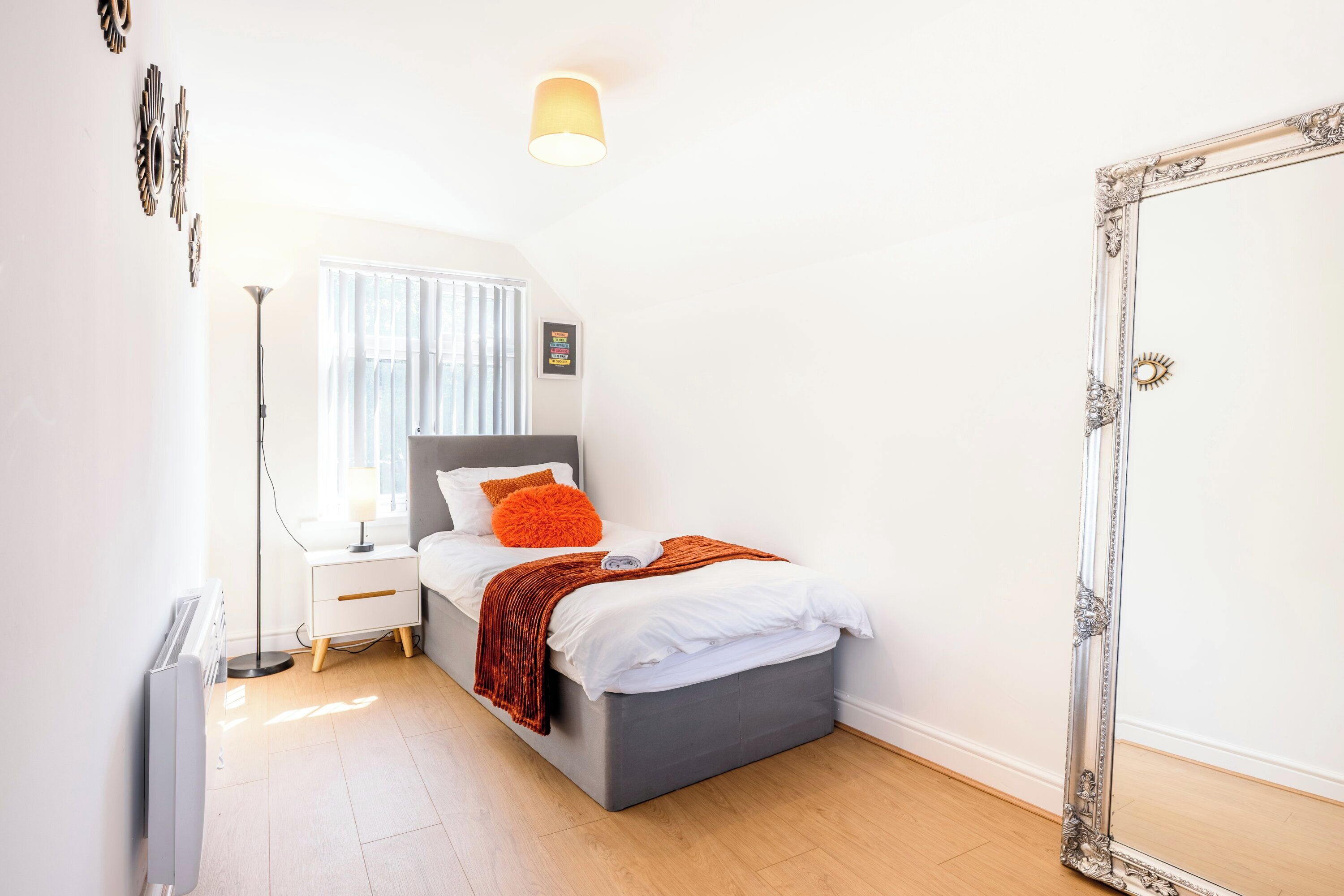 A bedroom with a bed, bedside table, lamp, and a large mirror.