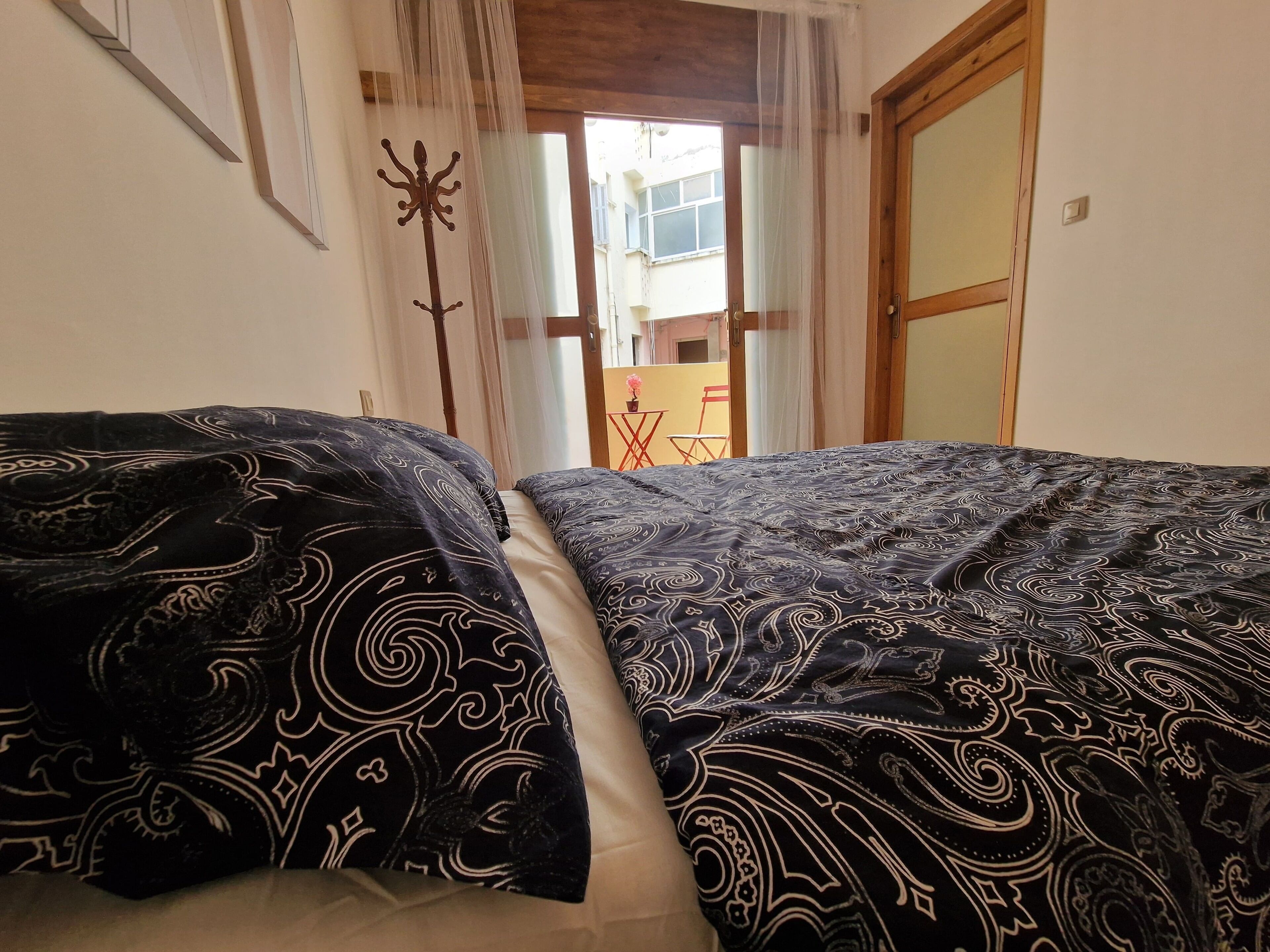 A room with a bed, a wooden door, and a view of the outside.