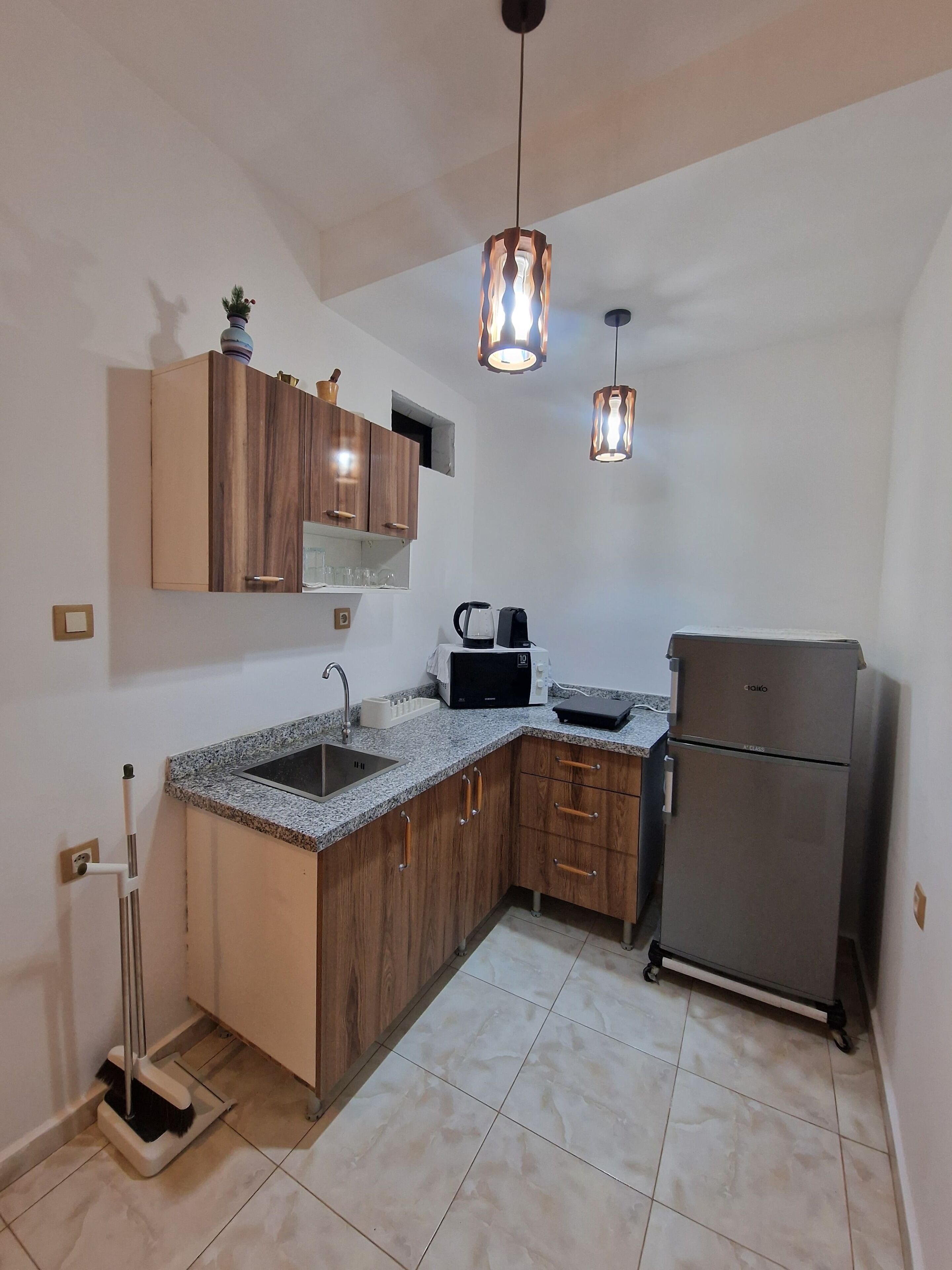 A compact kitchen with wooden cabinets, a built-in sink, a coffee maker, a toaster, and a refrigerator.