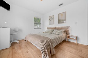 Ein Schlafzimmer mit Bett, Schreibtisch, Stuhl und einem Fenster mit Jalousien.