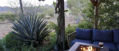 A covered outdoor seating area with a fire feature and a view of the desert landscape.