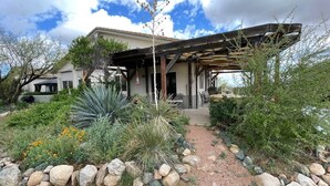 Ein modernes Haus mit überdachter Terrasse, umgeben von einem angelegten Garten mit verschiedenen Pflanzen und Steinen.