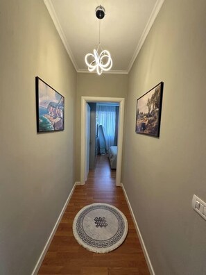 A hallway with a round rug, two framed pictures on the walls, a ceiling light fixture, and a door leading to another room. - Olive apartment by TOK (Durrës)