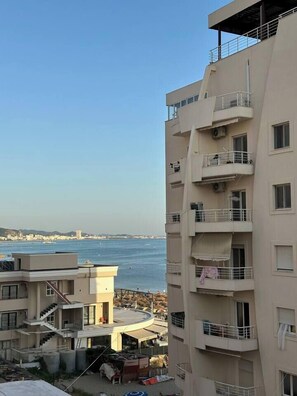 A multi-story building with balconies, a view of the sea, and a distant cityscape. - Olive apartment by TOK (Durrës)