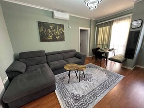 A living room with a grey sectional sofa, a small wooden table, and a patterned rug. - Olive apartment by TOK (Durrës)