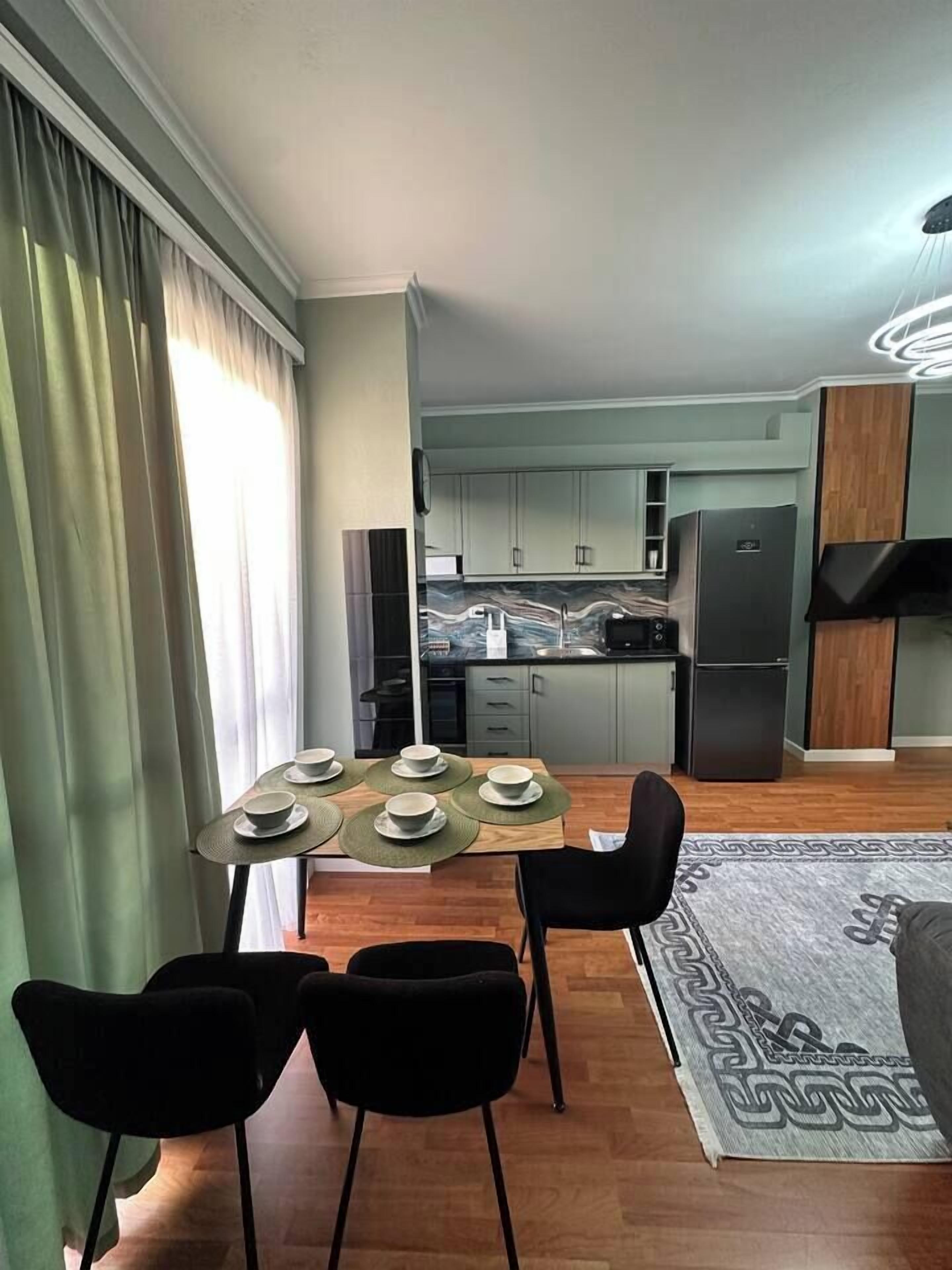 Una cocina moderna con un refrigerador negro, un microondas y una encimera de mármol. Se observa un comedor con una mesa preparada para cuatro personas, y una silla negra.