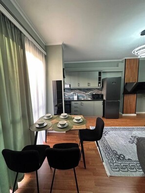 A modern kitchen with a black refrigerator, a microwave, and a marble countertop. There is a dining area with a table set for four, and a black chair is visible. - Olive apartment by TOK (Durrës)