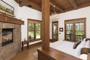A spacious bedroom with a stone fireplace, large windows, and a wooden ceiling. - 6-bedroom Ski-in/Ski-Out Luxury Mountain Retreat with Spanish Peaks Views (Big Sky)