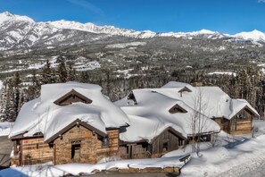 A row of log cabins with snow-covered roofs, set against a backdrop of snow-covered mountains and trees. - 6-bedroom Ski-in/Ski-Out Luxury Mountain Retreat with Spanish Peaks Views (Big Sky)
