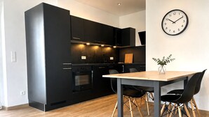 A modern kitchen with black cabinetry, a wooden dining table, and a wall clock. - Stylish dream apartment - 2 bedrooms - balcony (Bayreuth)