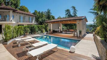 Une piscine avec des chaises longues, un patio couvert et une vue sur les montagnes.