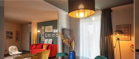 Un salon moderne avec une table ronde en verre, des fauteuils turquoise, un canapé rouge et un grand vase orné de branches décoratives.