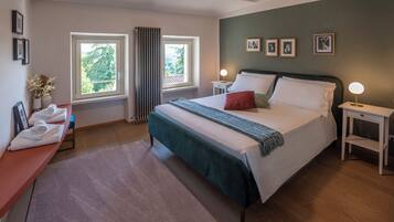Une chambre à coucher avec un lit, deux tables de chevet, une fenêtre, un banc avec des serviettes et des tableaux encadrés accrochés au mur.