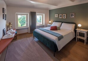 Ein Schlafzimmer mit einem Bett, zwei Nachttischen, einem Fenster, einer Sitzbank mit Handtüchern und gerahmten Bildern an der Wand.