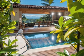 Un área de piscina con un deck de madera, una mesa con sillas y vistas al paisaje.