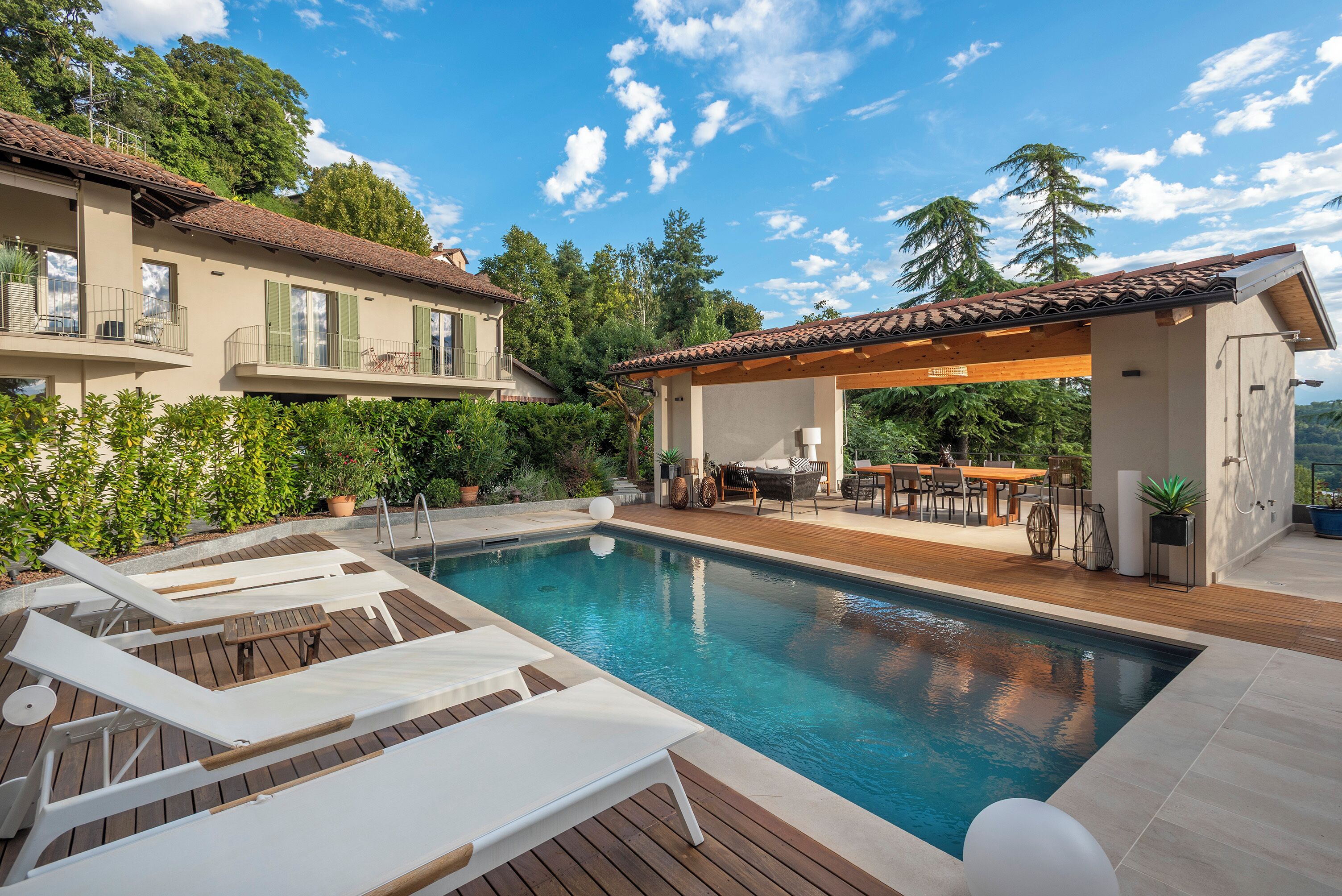 A swimming pool with lounge chairs, a wooden deck, and a covered outdoor dining area.