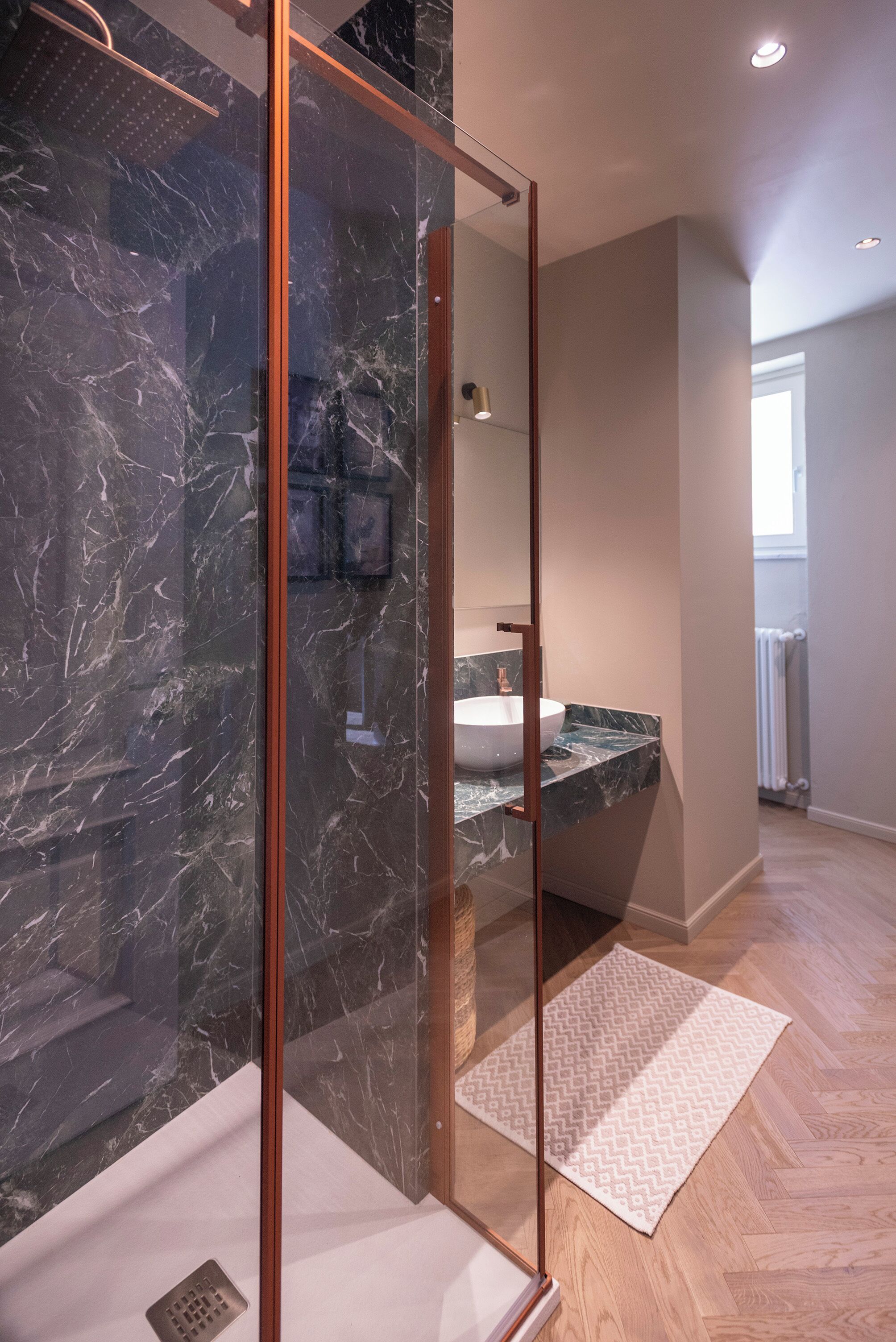 Een moderne badkamer met een glazen douchecabine, een marmeren aanrechtblad en een visgraat houten vloer.