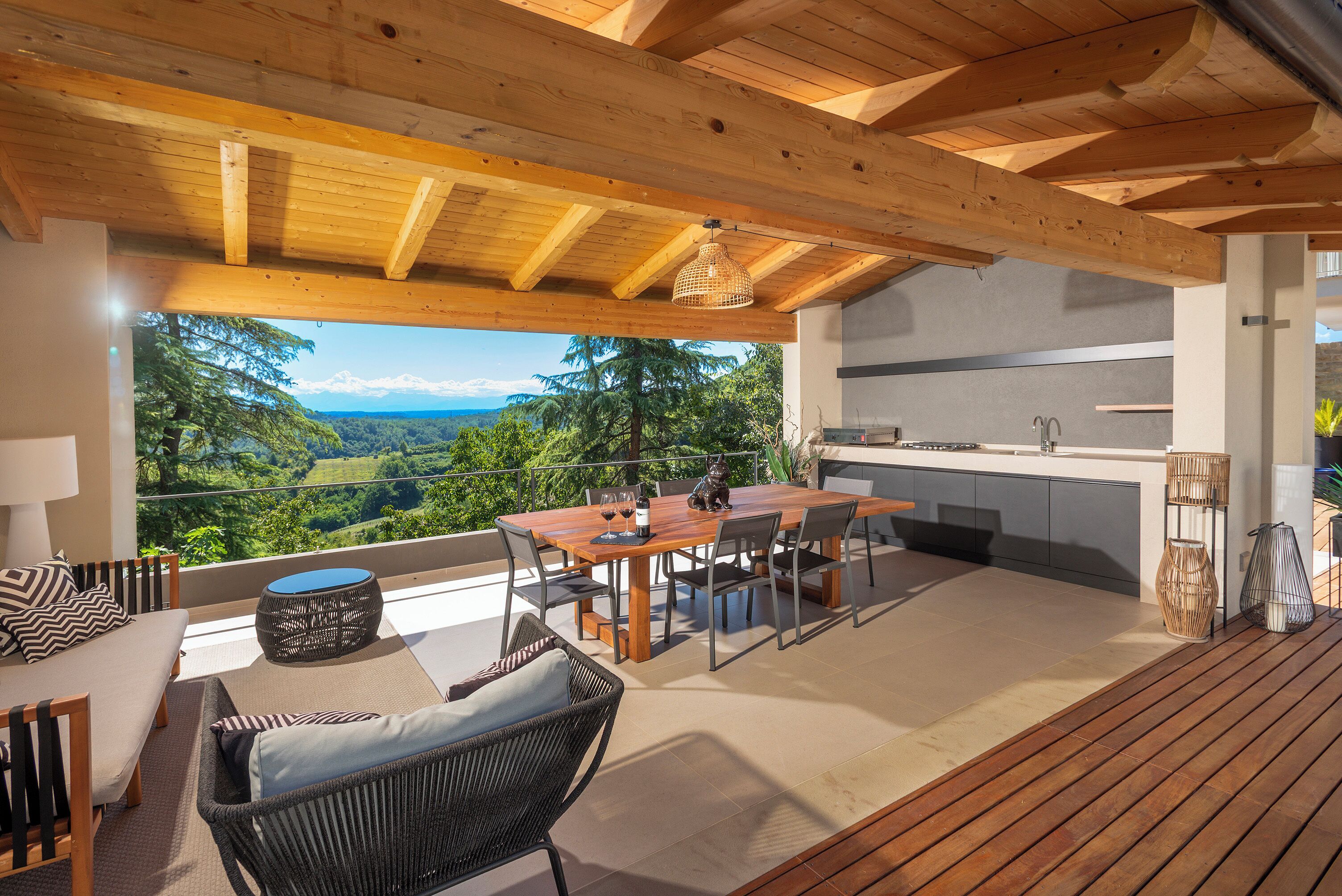 Una terraza de madera con zona de comedor, cocina y vistas a un paisaje montañoso.