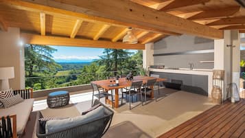Una terraza de madera con zona de comedor, cocina y vistas a un paisaje montañoso.