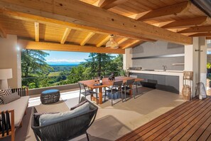 Eine Holzterrasse mit Essbereich, Küche und Blick auf eine gebirgige Landschaft.