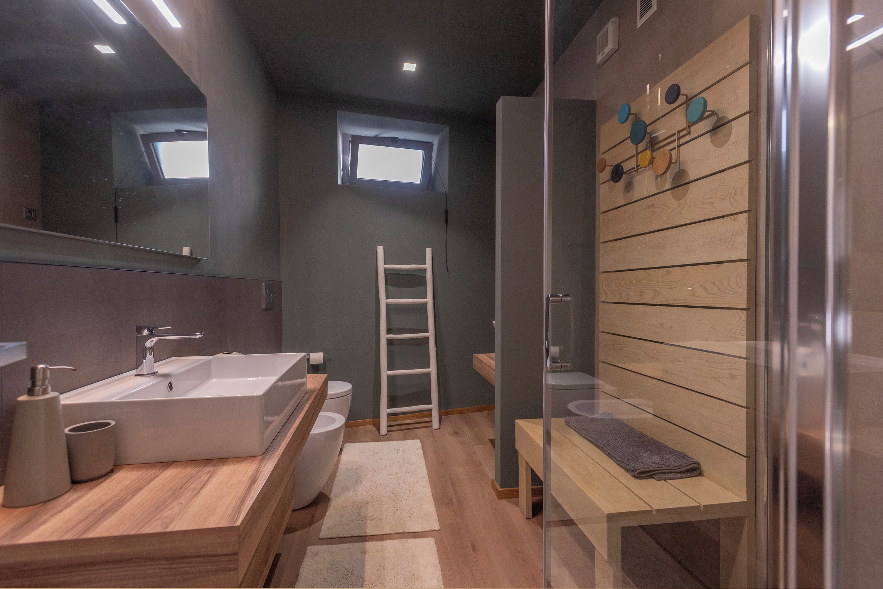 A modern bathroom with a large sink, a toilet, a ladder, and a bench.