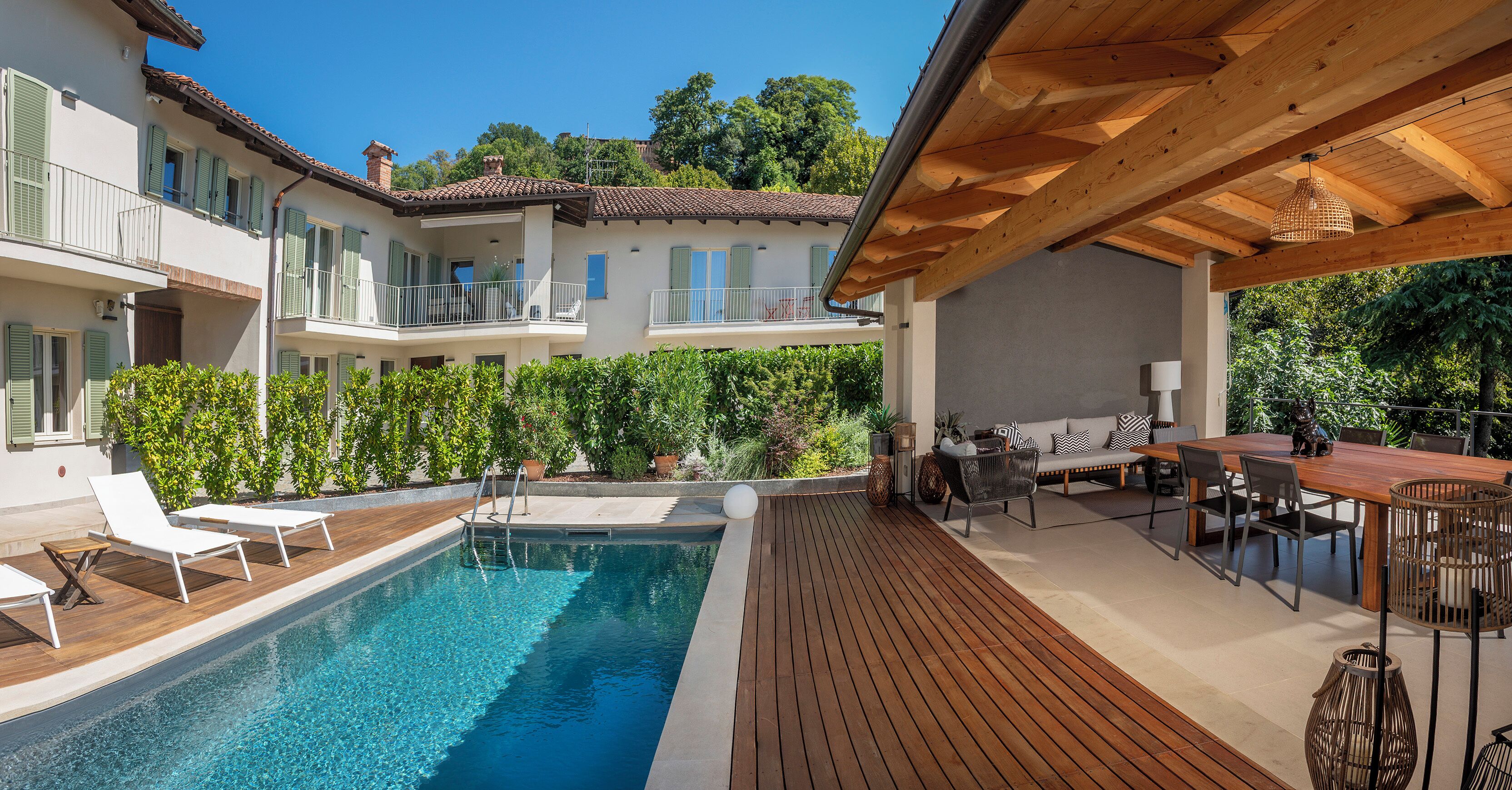 A poolside area with a wooden deck, lounge chairs, and a dining table with chairs.