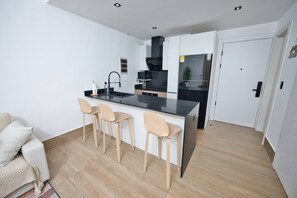 Eine moderne Küche mit schwarzem Arbeitsplatz, drei hölzernen Barhocker, einem weißen Sofa und einer weißen Tür.
