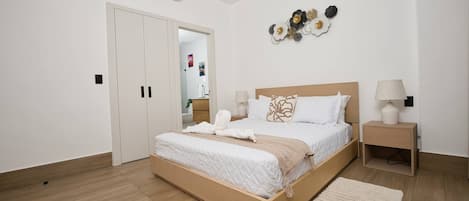 A modern bedroom with a wooden bed, white bedding, a bedside table with a lamp, and a wall-mounted air conditioner.