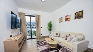 A modern living room with a sofa, a coffee table, a TV, and a balcony with curtains. - Modern Apartment With Private Pool in Punta Cana (Punta Cana)