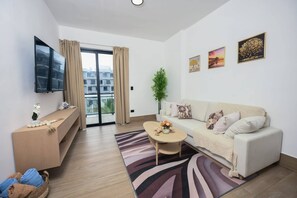 Ein modernes Wohnzimmer mit einer Couch, einem Couchtisch, einem Fernseher und einem Balkon mit Vorhängen.