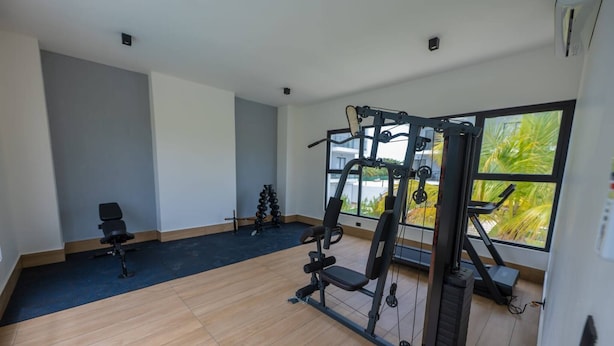 A gym with exercise equipment, a bench, and a large window with a view. - Modern Apartment With Private Pool in Punta Cana (Punta Cana)