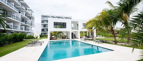 A modern hotel with a swimming pool, outdoor seating, and a well-maintained garden.