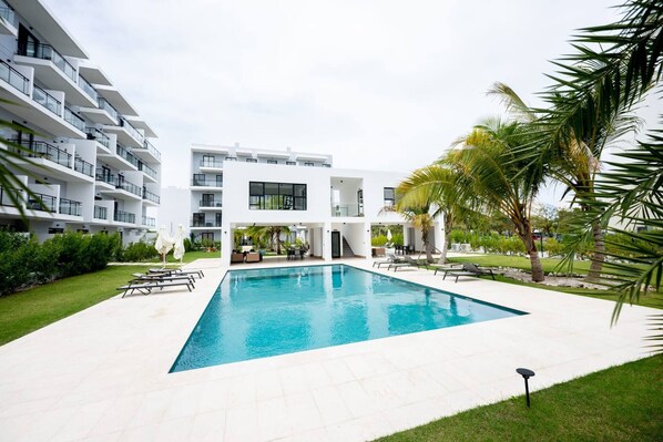 Un hotel moderno con piscina, zona de estar exterior y un jardín cuidado.
