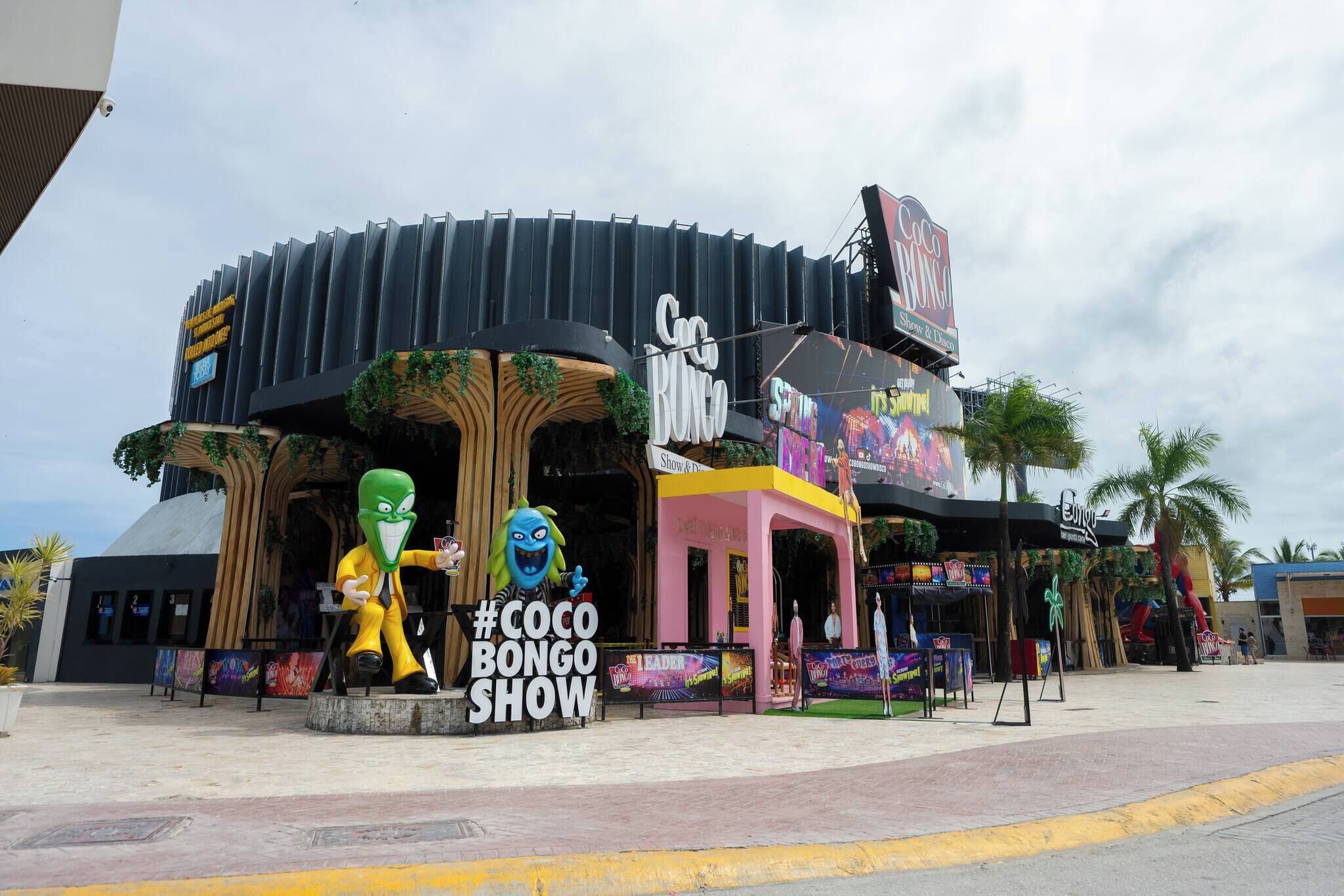 Ein Gebäude mit einem Schild für die 'Coco Bongo Show' und einer Maskottchenstatue.