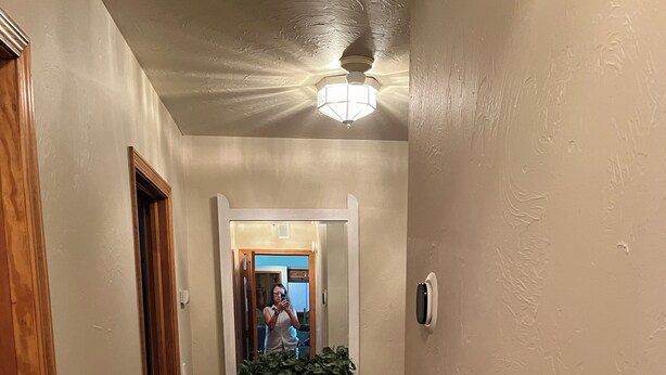 En smal hall med en trädörr på vänster sida, en vit bänk med gröna växter i mitten och en taklampa.