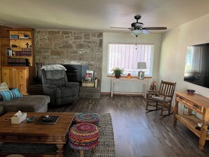 A living room with a fireplace, a ceiling fan, a television, and a bookshelf. - Classic lake lodge, boat launch, views, dock, blue water (Porum)