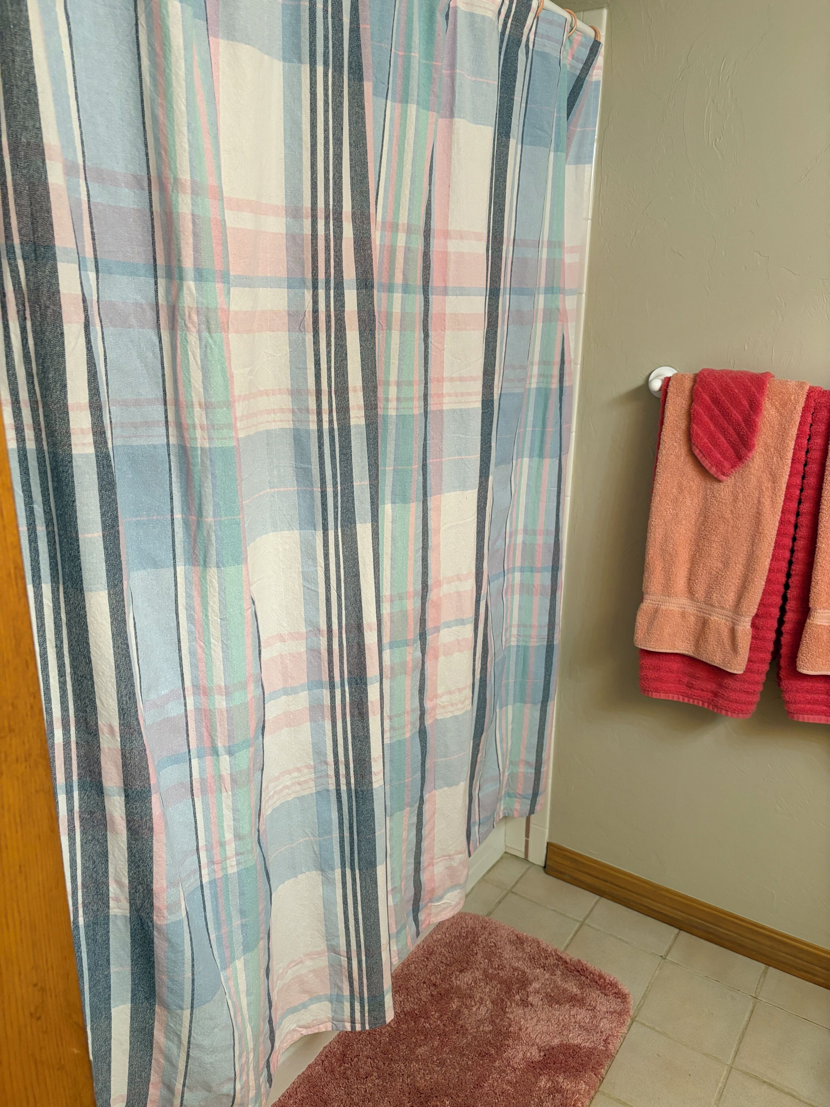 A bathroom with a plaid shower curtain, a pink rug, and two towels on a rack.