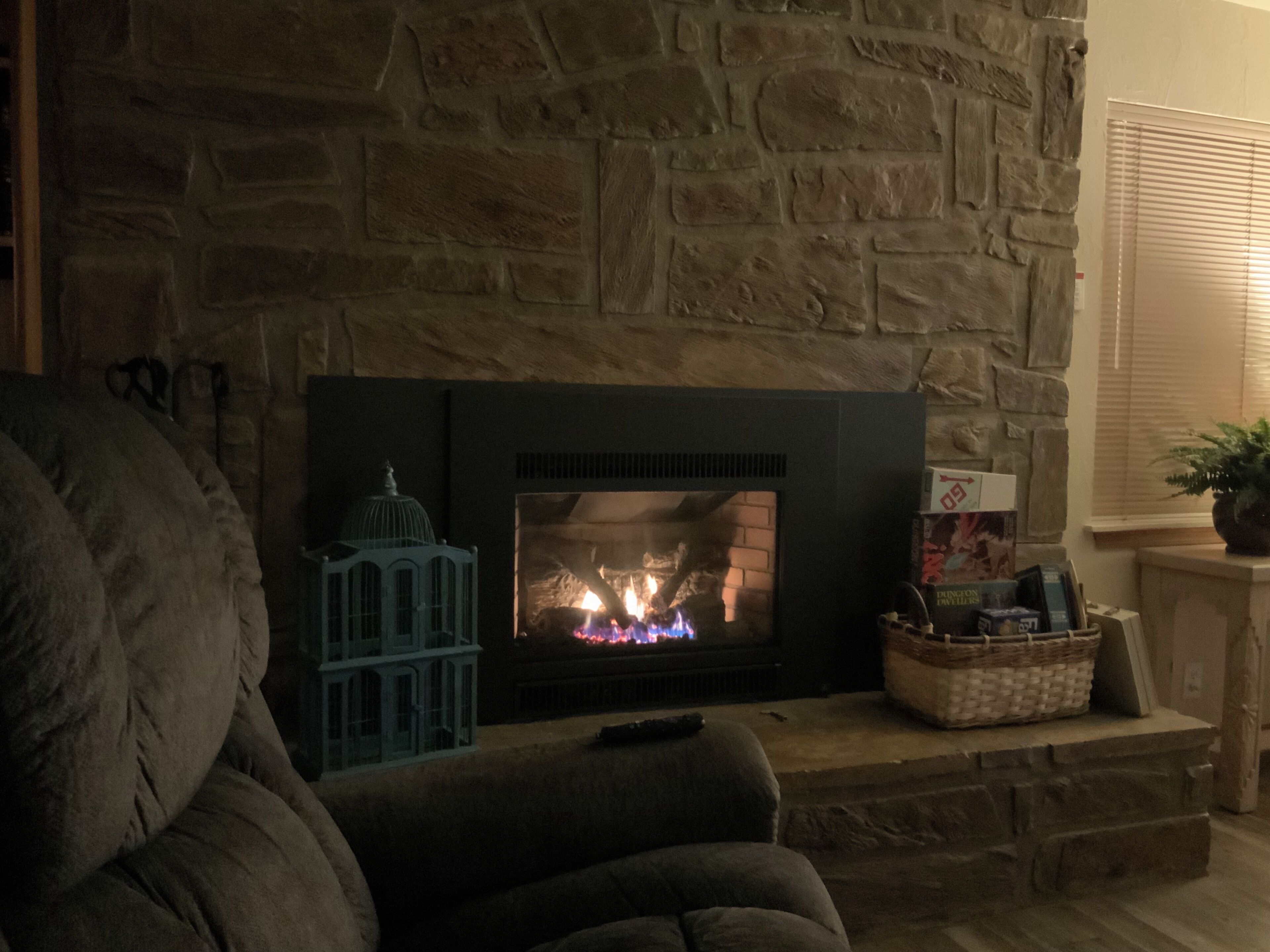 A stone fireplace with a fire, a blue decorative piece, and a basket with items on a mantel.