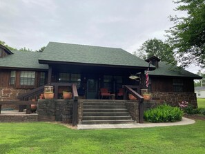 A rustic lodge with a stone facade, a porch with steps, and a flag. - Classic lake lodge, boat launch, views, dock, blue water (Porum)