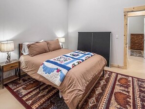 Ein Schlafzimmer mit einem Bett, Nachttischlampen, einem dunklen Kopfteil, einem gemusterten Teppich und einem Spiegel.