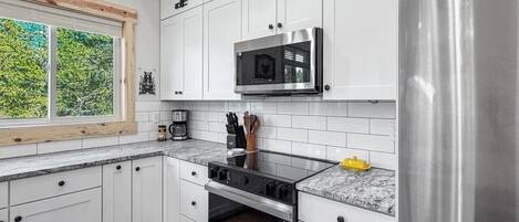 Una cocina moderna con armarios blancos, electrodomésticos de acero inoxidable y un ventanal con vistas a zonas verdes.