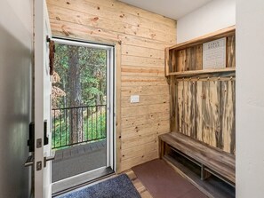A cabin interior with a wooden wall, a bench, and a door leading to a balcony with a view of trees. - Spacious 4BR Retreat on 1 Acre | Hot Tub, Pool Table & Near Lake Cascade (Cascade)