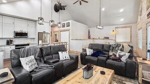 Un espacio moderno para vivir con cocina, dos sofás de cuero, una mesa de centro de madera y un ventilador de techo.