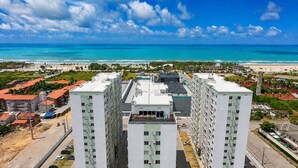 A high-rise building with multiple floors, surrounded by a coastal landscape with a beach and ocean. - Hosts BR - Apto no Mirante Clube (Fortaleza)